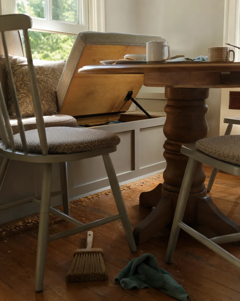 Breakfast bench storage lid blocked by the table while crumbs and cleaning tools remain visible below.