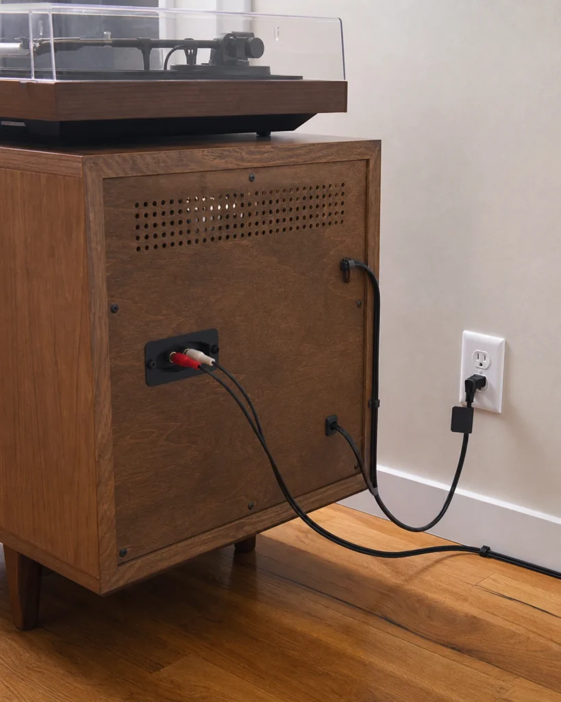 Rear view of record-player components with accessible cables following the back of the cabinet and wall.